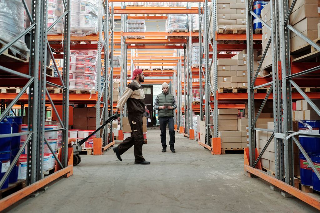 Two workers in a warehouse aisle between tall pallet racks
